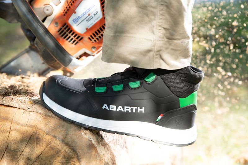 Ein Arbeiter trägt schwarzen ABARTH Sicherheitsschuh mit grünen Ösen und weißer Sohle während Holzarbeiten mit Motorsäge.