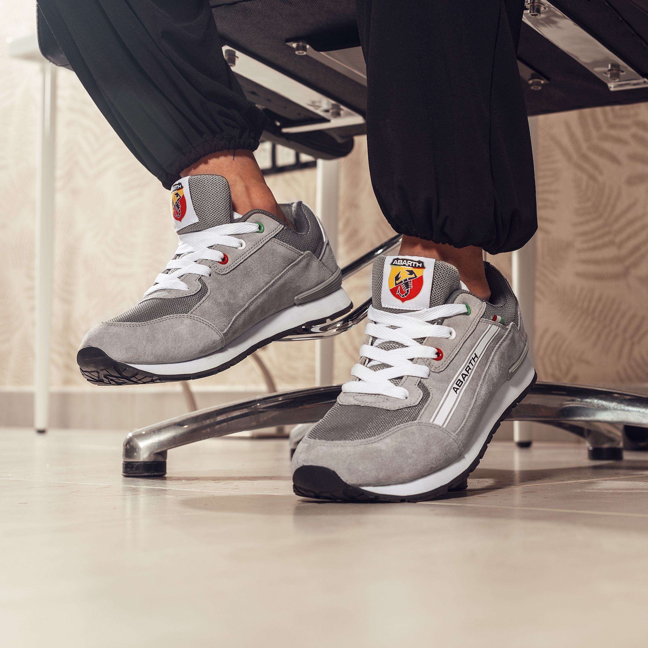 Seitliche Ansicht eines grauen ABARTH Arbeitsschuhpaars im sportlichen Sneaker-Design mit robuster schwarzer Laufsohle, weißer Schnürung, seitlichem ABARTH-Schriftzug und italienischen Flaggen-Details.