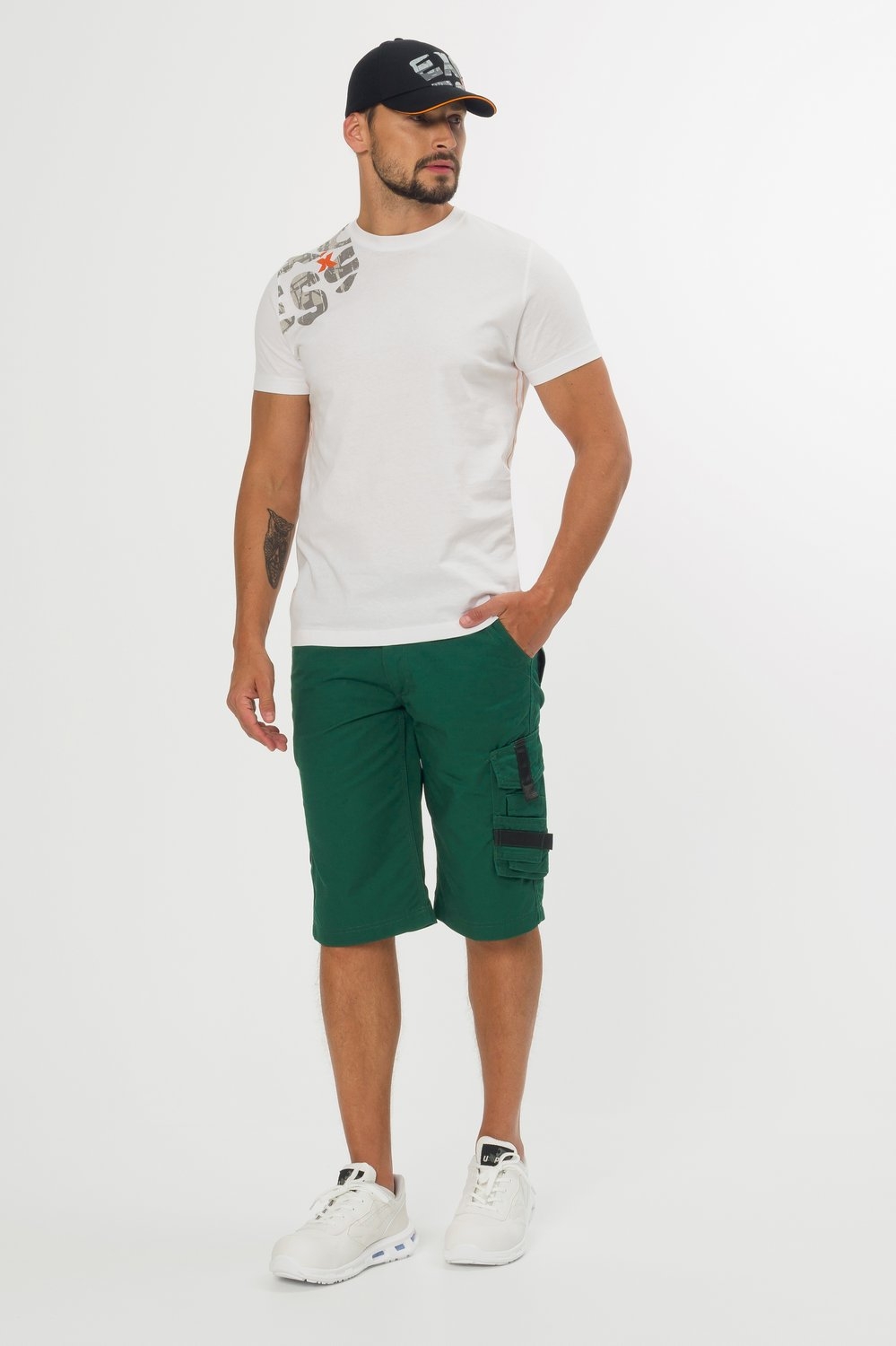 Grüne Arbeitsshorts mit schwarzen Taschen – kombiniert mit weißem T-Shirt, Sneakern und Cap, moderne Berufsmode.
