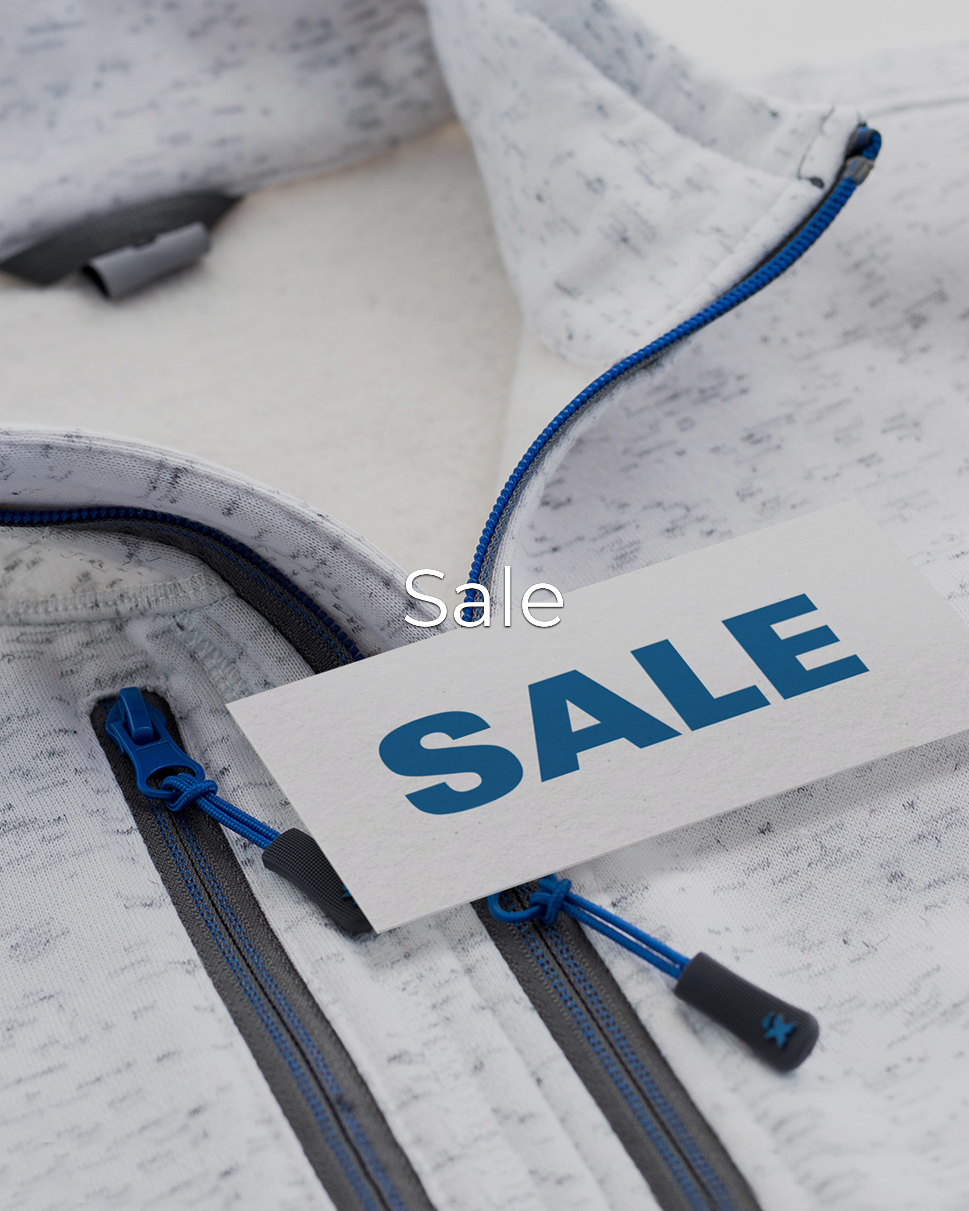 Nahaufnahme einer hellen Jacke mit blauen Reißverschlüssen und einer weißen Karte mit der Aufschrift „SALE“. In der Bildmitte steht zusätzlich der Schriftzug „Sale“.