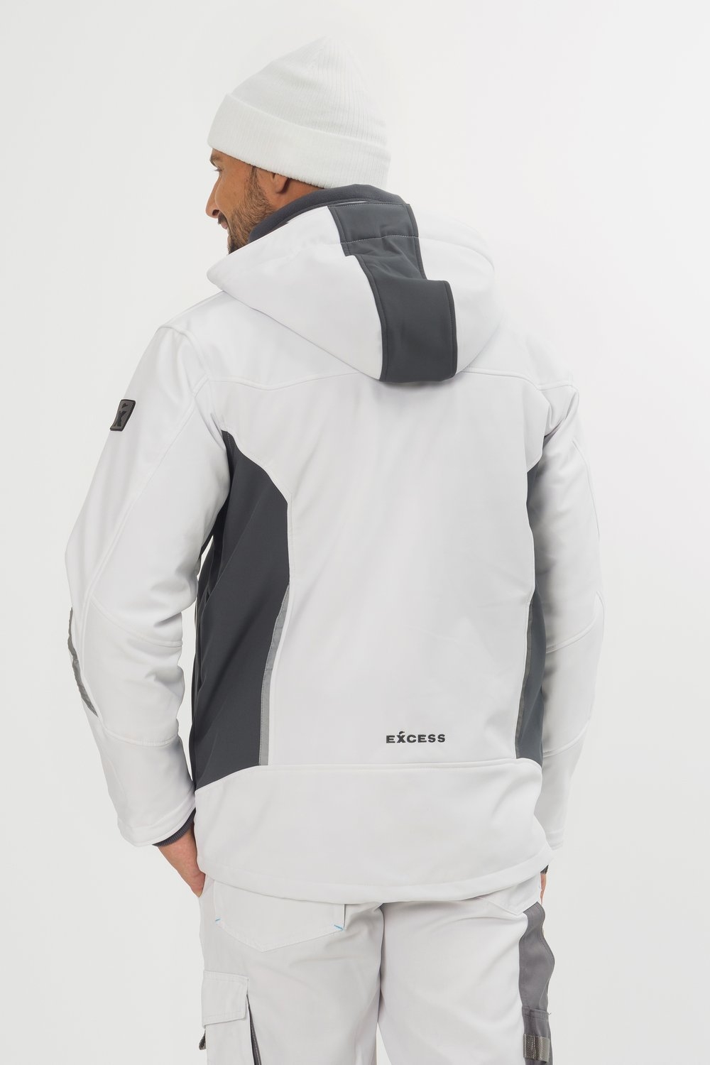 Rückansicht einer weißen Softshelljacke von Excess Workwear, getragen von einem Modell. Die Jacke hat graue Einsätze, eine Kapuze, ein Logo am unteren Rücken sowie ergonomischen Schnitt. Kombiniert mit passender Arbeitshose und Mütze.