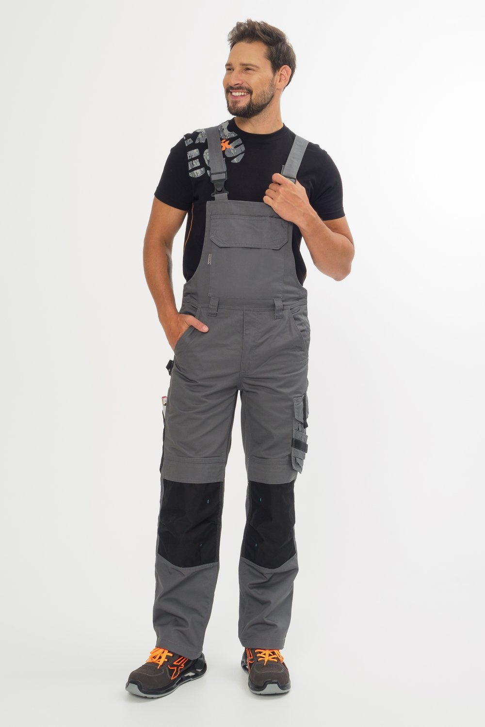 Graue Latzhose mit schwarzen Knieverstärkungen und vielen Taschen – strapazierfähige Arbeitslatzhose für Handwerker und Bau.