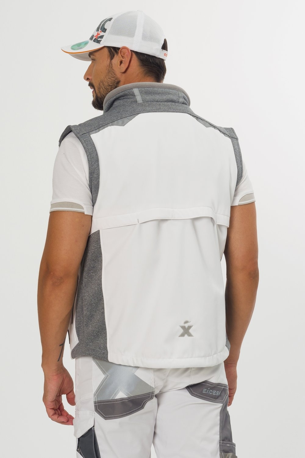 Rückansicht eines Mannes in weiß-grauer Softshell-Arbeitsweste von Excess mit Belüftungsfalte am Rücken, grauen Schulter- und Seiteneinsätzen sowie reflektierendem Logo, kombiniert mit passender Arbeitshose und Cap.