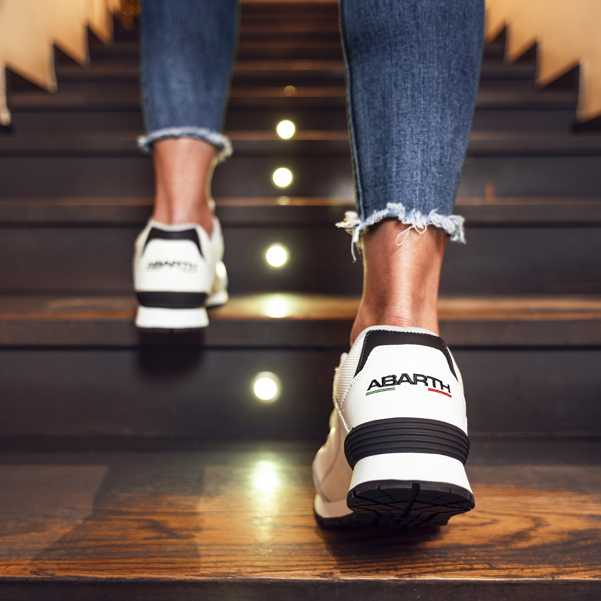 Abarth Sneaker weiß mit schwarzem Detail, sportliche Schuhe beim Treppensteigen in moderner Umgebung.